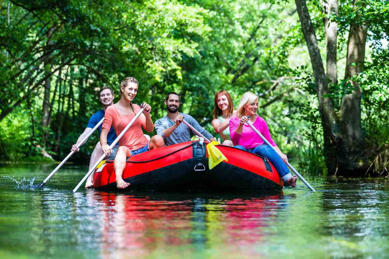 Friends paddling on rubber boat at forest river or creek
